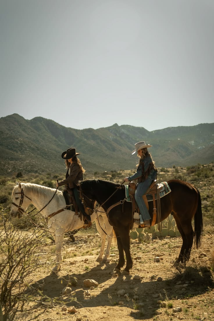 Duas mulheres de chapéu montando cavalos diante das montanhas
