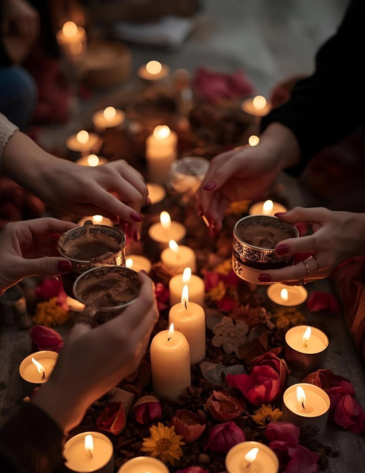 Mãos segurando xícaras em um círculo noturno iluminado por velas e pétalas